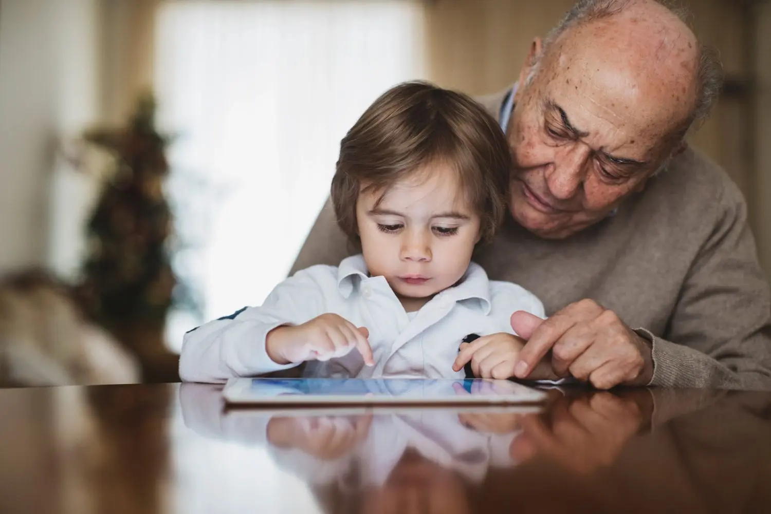 Grandpa is playing with his granddaughter who is using a tablet