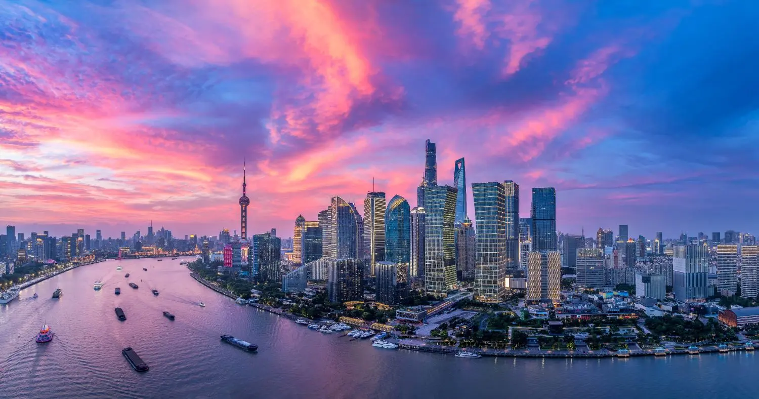 A panoramic view of the Shanghai skyline featuring modern skyscrapers, the iconic tower, boats, and a blend of urban and natural scenery.