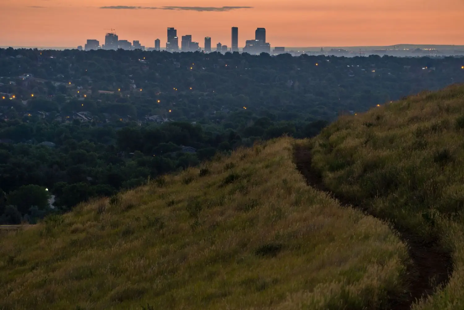 A beautiful sunrise over Denver, Colorado with a cityscape on the urban slope, surrounded by verdant grassland and a meandering path.