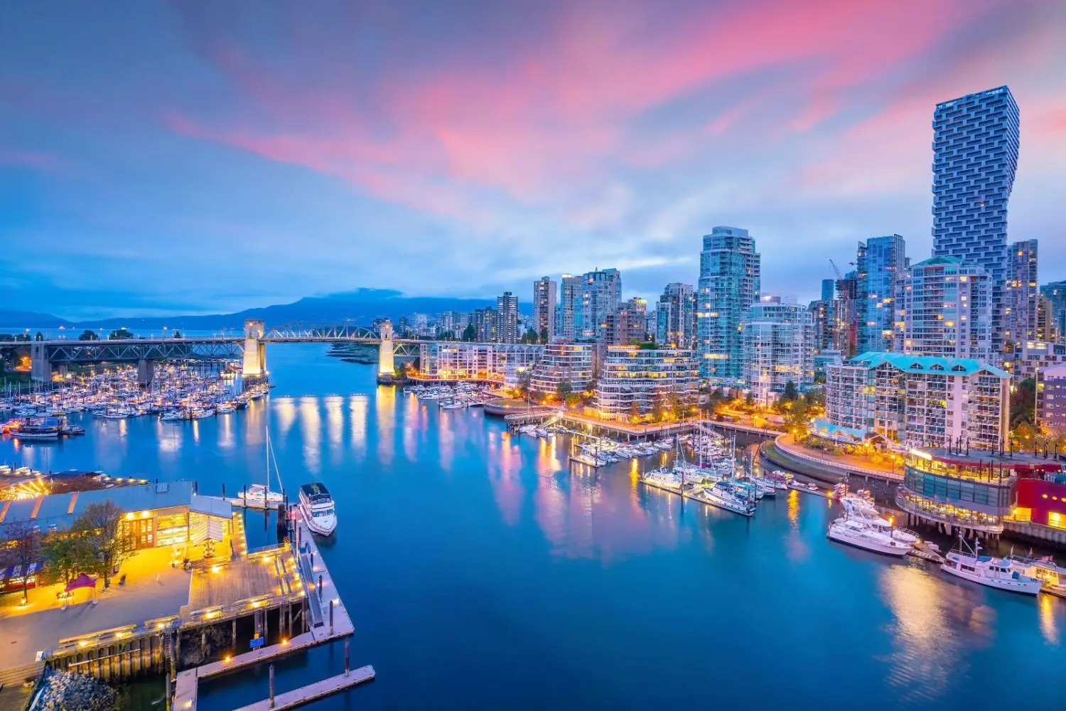 Stunning evening city view of Vancouver with illuminated skyscrapers, waterfront, boats in the harbor, reflecting on the serene water.