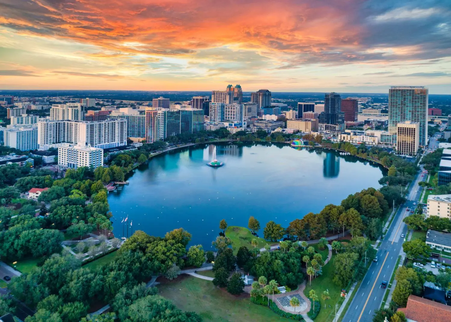 Aerial view of Orlando, Florida featuring a scenic lake, urban cityscape, buildings, cars, and lush natural surroundings