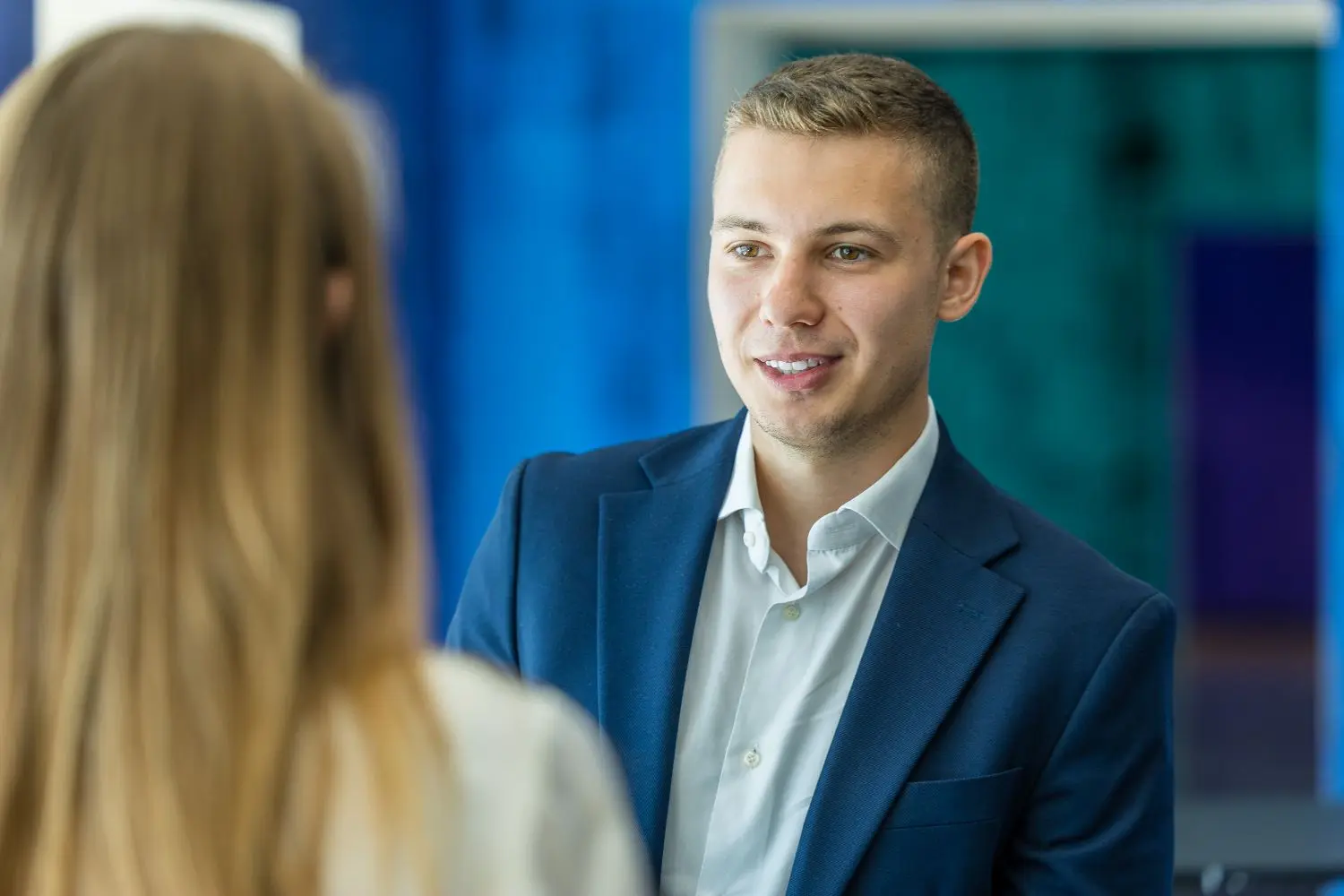 A smiling adult man in a blazer and shirt engaged in a conversation, showcasing a confident and professional demeanor.